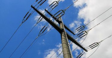 Betonski elektroenergetski stup sa više visokonaponskih vodova protiv plavog neba
