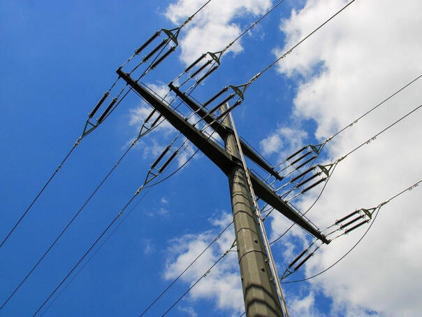 Betonski elektroenergetski stup sa više visokonaponskih vodova protiv plavog neba