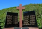 Memorijalni križ s imenima žrtava na zeleni brežuljku, posvećen žrtvama iz Trusine