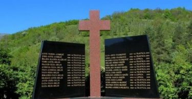 Memorijalni križ s imenima žrtava na zeleni brežuljku, posvećen žrtvama iz Trusine