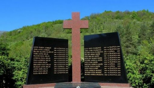 Memorijalni križ s imenima žrtava na zeleni brežuljku, posvećen žrtvama iz Trusine
