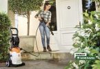 Žena koristi visokotlačni perač za čišćenje betonske terase ispred kuće