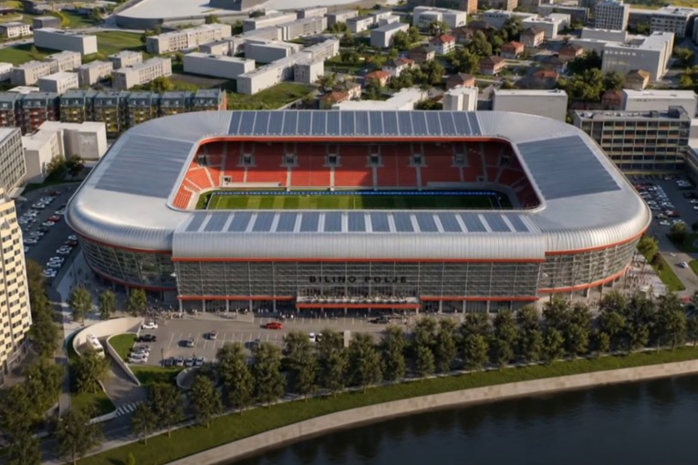 Moderni stadion s crvenim i plavim sjedalima uz obalu rijeke u urbanom okruženju