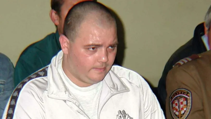 Muško lice tokom sudskog ročišta, u bijeloj majici i tamnoj uniformi u pozadini