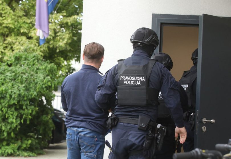 Policajci prate muškarca u tamnoj odjeći prema vratima zgrade tijekom sudskog postupka