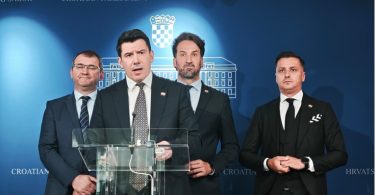 Četiri muškarca u odijelima pri govornskom pultu tijekom parlamentarne konferencije