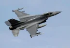 Vojni avion F-16 u letu snimljen iz donje perspektive protiv plavog neba