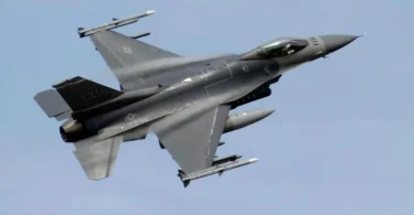 Vojni avion F-16 u letu snimljen iz donje perspektive protiv plavog neba