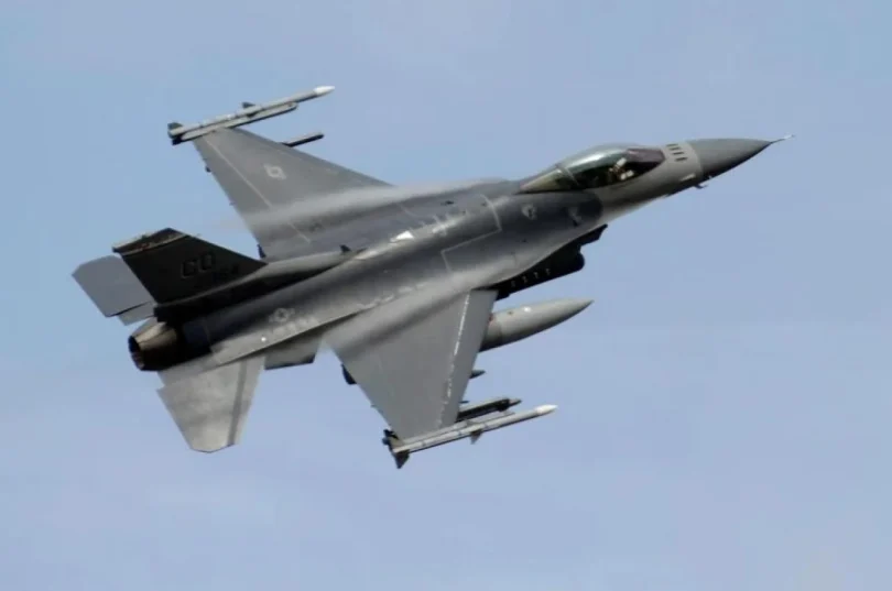 Vojni avion F-16 u letu snimljen iz donje perspektive protiv plavog neba