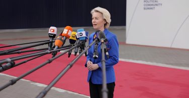 Žena u plavoj jakni govori pred mikrofonima na konferenciji o trgovinskim pregovorima