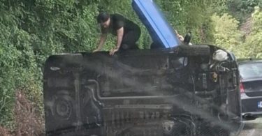 Prevrnuti crni automobil na cesti, spasioci izvlače ljude iz vozila
