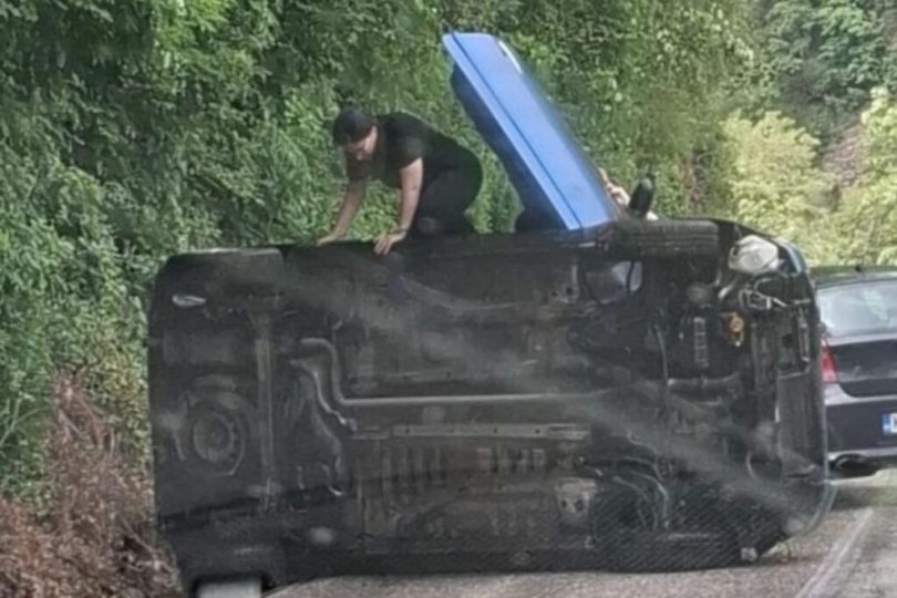Prevrnuti crni automobil na cesti, spasioci izvlače ljude iz vozila