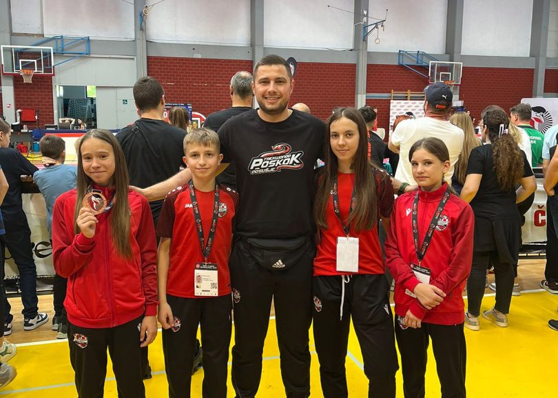 Grupa mladih karatista u crvenim kimona-ma s trenerom na sportskoj dvorani